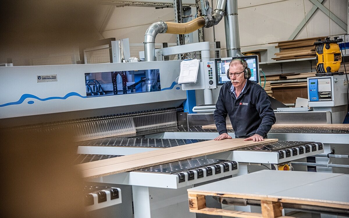 Man aan het werk bij een CNC-machine in de fabriek van Van Keulen Interieurbouw, waar houten onderdelen worden gezaagd voor meubelproductie.