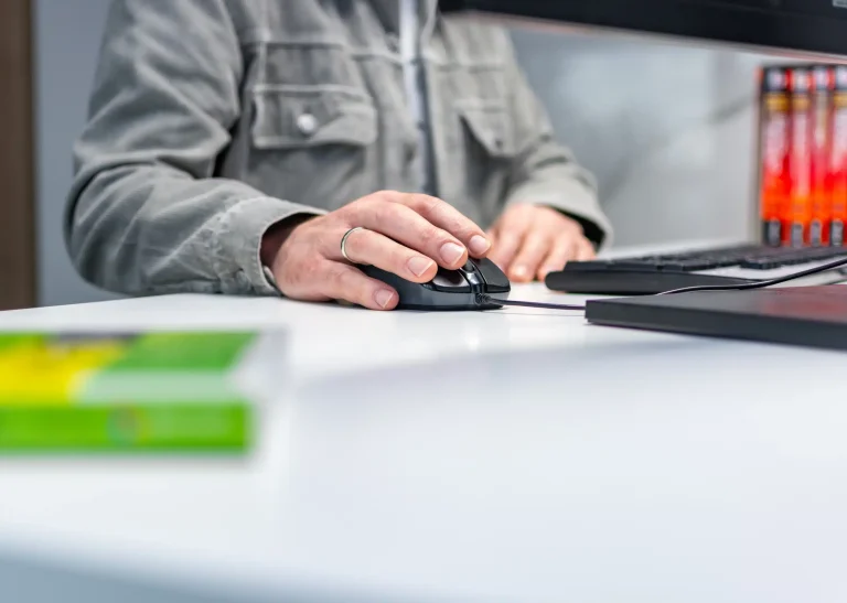Close-up van een werkvoorbereider die met een computermuis werkt aan een bureau met toetsenbord en monitor