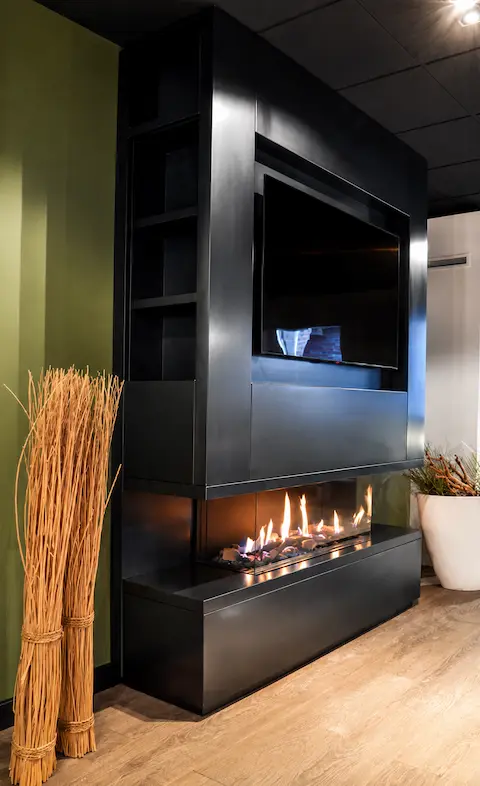 Moderne zwarte cinewall met ingebouwde haard en televisie, sfeervol verlicht in een strak interieur met houten vloer en warme natuurlijke accenten.”