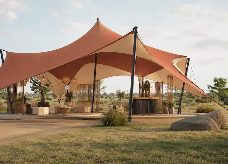 Stretchtent met meerdere hoge punten, warme terracotta- en zandtinten en donkere steunpalen, opgesteld als stijlvolle open evenementenruimte in een natuurlijke buitenomgeving.